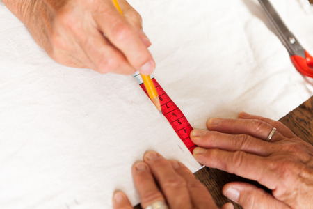 Hand Cutting Cloth with Scissors with Measuring Tape and Pencil Nearby
