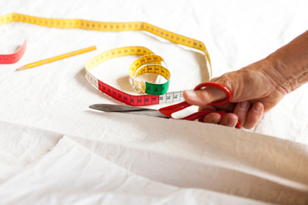 Hand Cutting Cloth with Scissors with Measuring Tape and Pencil Nearby