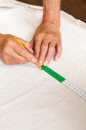 Hand Cutting Cloth with Scissors with Measuring Tape and Pencil Nearbyの写真素材