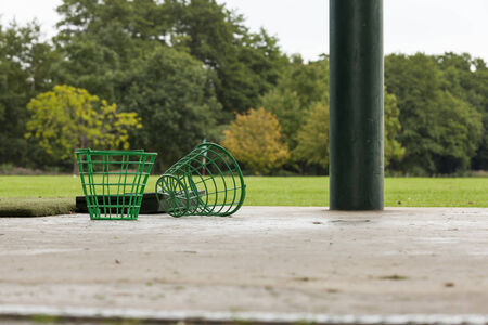 Two Empty Golf Ball Baskets at Driving Range with Hole and Flag in Backgroundの写真素材
