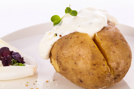 Overhead view of a healthy oven baked jacket potato with sour cream sauce garnished with endive leaves and fresh herbsの写真素材