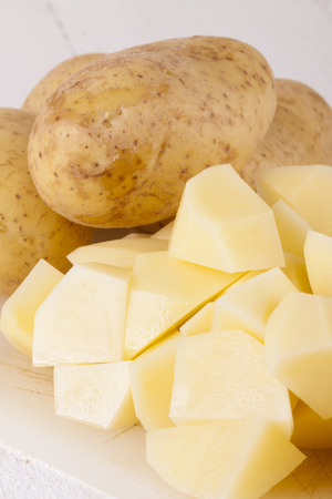 Three Whole Potatoes and Chopped Peeled Pieces on cutting boardの写真素材