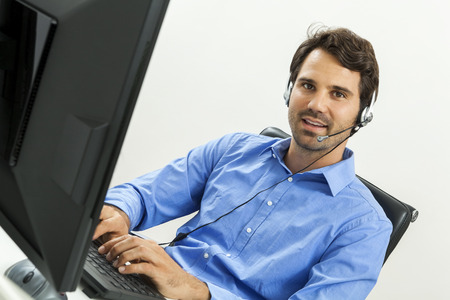 Attractive unshaven young man wearing a headset offering online chat and support on a client...
