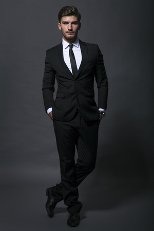 Handsome bearded young businessman in a stylish suit adjusting his tie with a serious thoughtful expressionの写真素材