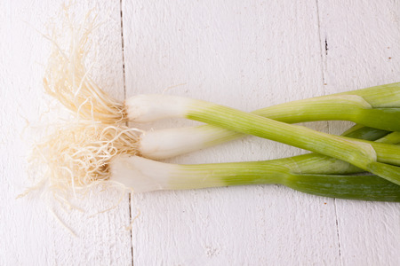 Overhead view of a bunch of fresh leafy leeks or scallions lying on white painted wooden boardsの写真素材
