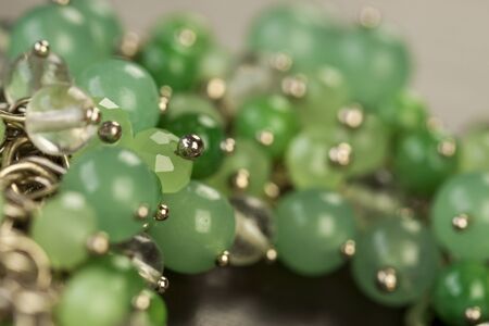 Close up view of pretty translucent green beads on an item of silver jewellery attached in a bunch to a ring by short chains with shallow dof in a fashion conceptの写真素材