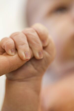 Tender love of a newborn infant with a closeup view of the hand of a tiny neonate clutching the finger of its parent in a show of trust, dependency and loveの写真素材