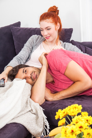 Young Couple Relaxing on the Couch In the Living Room, with Pensive Facial Expressions, While Boyfriend is Lying on the Lap of her Girlfriend.の写真素材