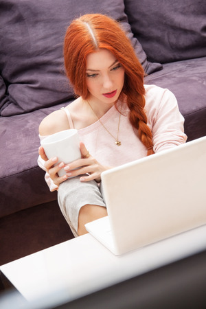 Pretty Young Woman Using her Laptop Computer In the Living Room with Feet on the Table and Showing Serious Face.の写真素材