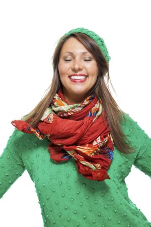 Cute young woman with long brunette hair in a green winter outfit smiling playfully at the camera with her hand to her red scarf, on whiteの写真素材