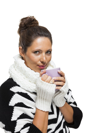 Cold attractive stylish woman in an elegant black and white winter outfit clasping a mug of hot coffee in her hands while savoring the aroma with a look of anticipationの写真素材