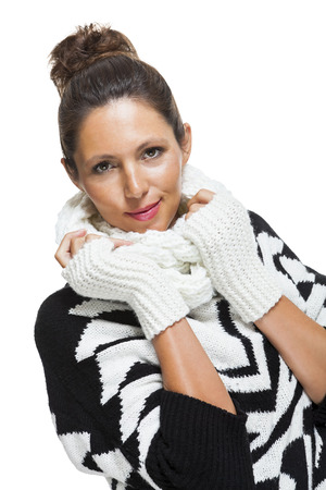Attractive elegant woman in winter fashion snuggling down into her white scarf and black and white jumper to ward off the cold winter weather, on whiteの写真素材