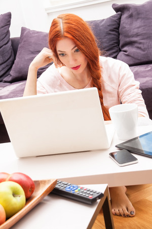 Pretty Young Woman Using her Laptop Computer In the Living Room with Feet on the Table and Showing Serious Face.の写真素材