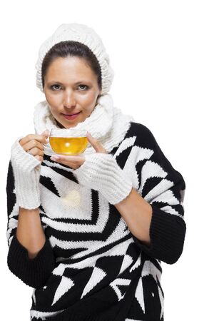Elegant woman in a stylish black and white winter outfit with matching white mitts, scarf and knitted hat drinking a cup of hot tea, isolated on whiteの写真素材