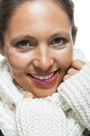 Attractive elegant woman in winter fashion snuggling down into her white scarf and black and white jumper to ward off the cold winter weather, on whiteの写真素材