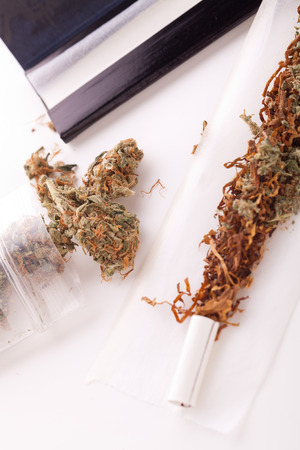 Close up Dried Cannabis Leaves on a Resealable Cellophane Wrapper and a Rolling Paper with Filter on Top of the Tableの写真素材