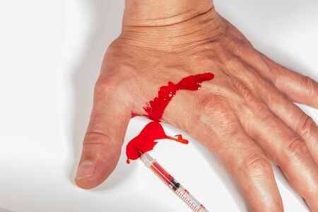 Subcutaneous medical injection concept with a small hypodermic syringe filled with a red liquid penetrating the skin and producing a flow of dripping blood in a close up viewの写真素材