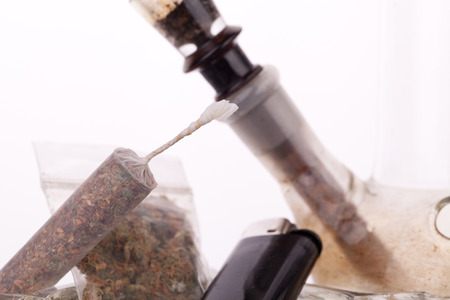 Close up of marijuana joint made with translucent rolling papers, plastic baggy of dried marijuana, black lighter and pipe on white backgroundの写真素材