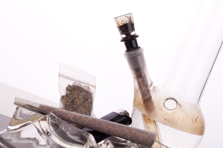 Close up of marijuana joint made with translucent rolling papers, plastic baggy of dried marijuana, black lighter and pipe on white backgroundの写真素材