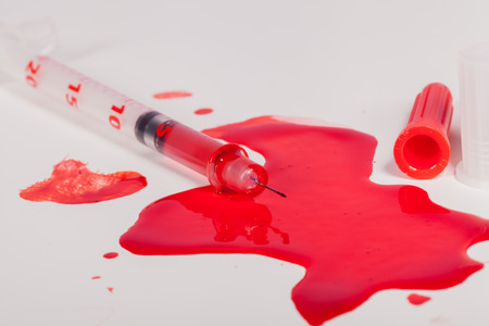 High Angle View of Syringe Needle Squirting Red Liquid or Blood onto White Background in Studio Still Life - Concept Imageの写真素材