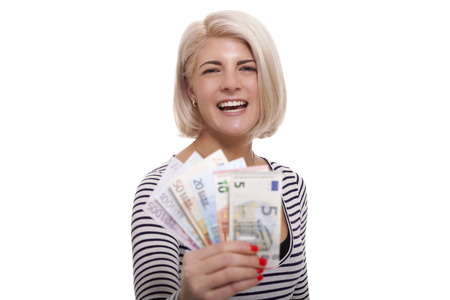 Attractive smiling blond woman holding up a handful of fanned Euro notes in different denominations, tilted angle conceptual image isolated on whiteの写真素材