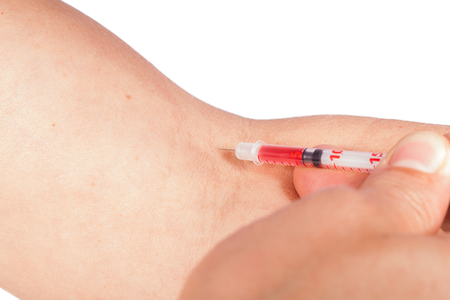 Subcutaneous medical injection concept with a small hypodermic syringe filled with a red liquid penetrating the skin and producing a flow of dripping blood in a close up viewの写真素材