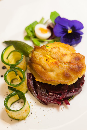 Delicious gourmet plate featuring biscuit sandwich with beets, zucchini strips and pansy garnish over white backgroundの写真素材