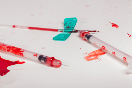 Concept Image - Surgical Aftermath Image of Needle Syringes and IV Lines Covered with Red Blood on White Background in Studio Still Lifeの写真素材