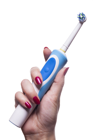 Hand with manicure holds single blue electric toothbrush against white backgroundの写真素材
