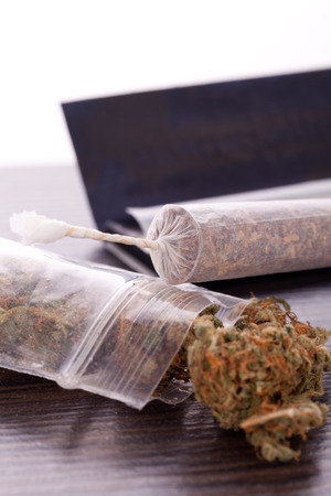 Close up Dried Cannabis Leaves on a Resealable Cellophane Wrapper and a Rolling Paper with Filter on Top of the Tableの写真素材