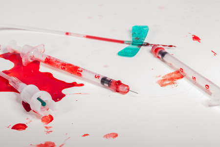 Concept Image - Surgical Aftermath Image of Needle Syringes and IV Lines Covered with Red Blood on White Background in Studio Still Lifeの写真素材