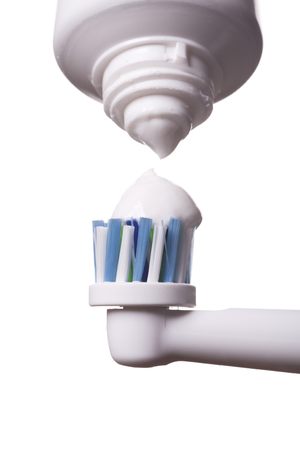 Close up of electric toothbrush with blue bristles and tube with paste bubbled at its opening on white backgroundの写真素材