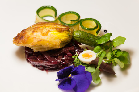 Delicious gourmet plate featuring biscuit sandwich with beets, zucchini strips and pansy garnish over white backgroundの写真素材