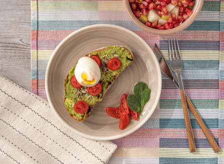 avocado toast with egg and a side bowl with fruits, on a table in a top view.の写真素材