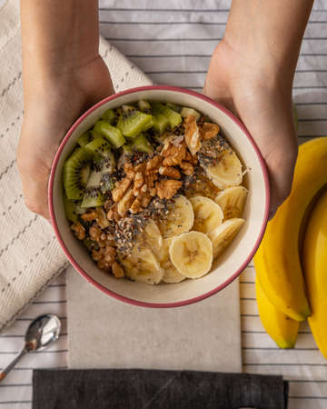 Hands holding a bowl with a porridge with kiwi, walnuts and banana.の写真素材