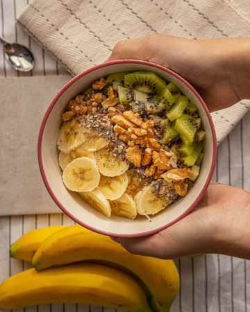 hands holding a porridge with banana, walnuts and kiwi.の写真素材
