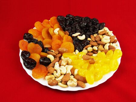 Dried fruits with nuts on the white plate on the red backgroundの写真素材