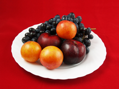 Fresh fruits on the white plate on the red backgroundの写真素材