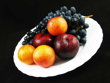 Fresh fruits on the white plate on the black backgroundの写真素材