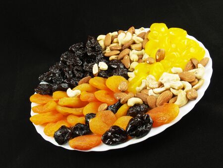 Dried fruits with nuts on the white plate on the black backgroundの写真素材