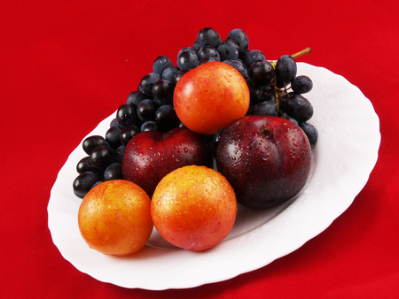 Fresh fruits on the white plate on the red backgroundの写真素材