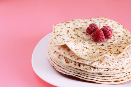 Fried pancakes close-up on a white plate, pancakes with raspberries, dessert on a pink background,...