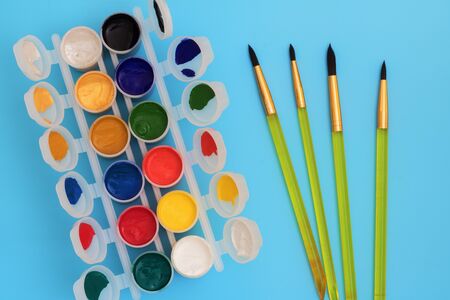 Colorful paints in jars on a blue background near the brushes. Color palette. Concept-creativity and school theme. Open cans of gouache paint are near Kitami to ratowania. copy spaceの写真素材