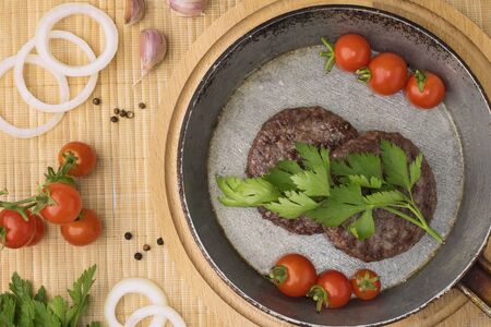 Fried Ground beef meat Burger steak cutlets in a cast iron pan on a wooden board background. Cutlet for burger with vegetables and spices. fast foodの写真素材