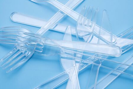 Plastic disposable tableware, cutlery. Fast food. Clean plastic forks and knives on blue background. Disposable dishes, environmental pollution. Top view, flat lay.の写真素材