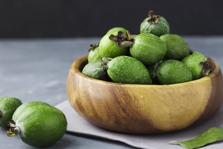 Green feijoa fruits in a wooden plate on a dark background. Tropical fruit feijoa.の写真素材