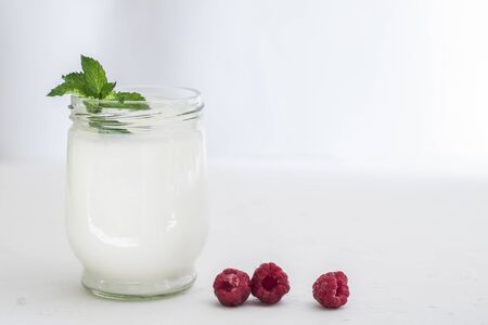 Organic probiotic milk kefir drink or yogurt in glass containers, with raspberry, on the white grey background. Gut health. Probiotic cold fermented dairy drink. Trendy food and drink. Copy spaceの写真素材