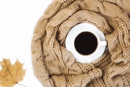 Cup black coffee on saucer with autumn maple leave next to the knitted scarf on a white concrete...