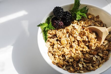 Blackberry with mint leaves, in a plate with granola with milk, on a white background with hard shadows. Selective focus. Copy spaceの写真素材