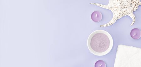 Cosmetic clay on lilac pink background, next to a towel, sea shell and with candles. The concept banner of beauty cosmetic procedures, spa, skin treatment and skin care. Copy spaceの写真素材
